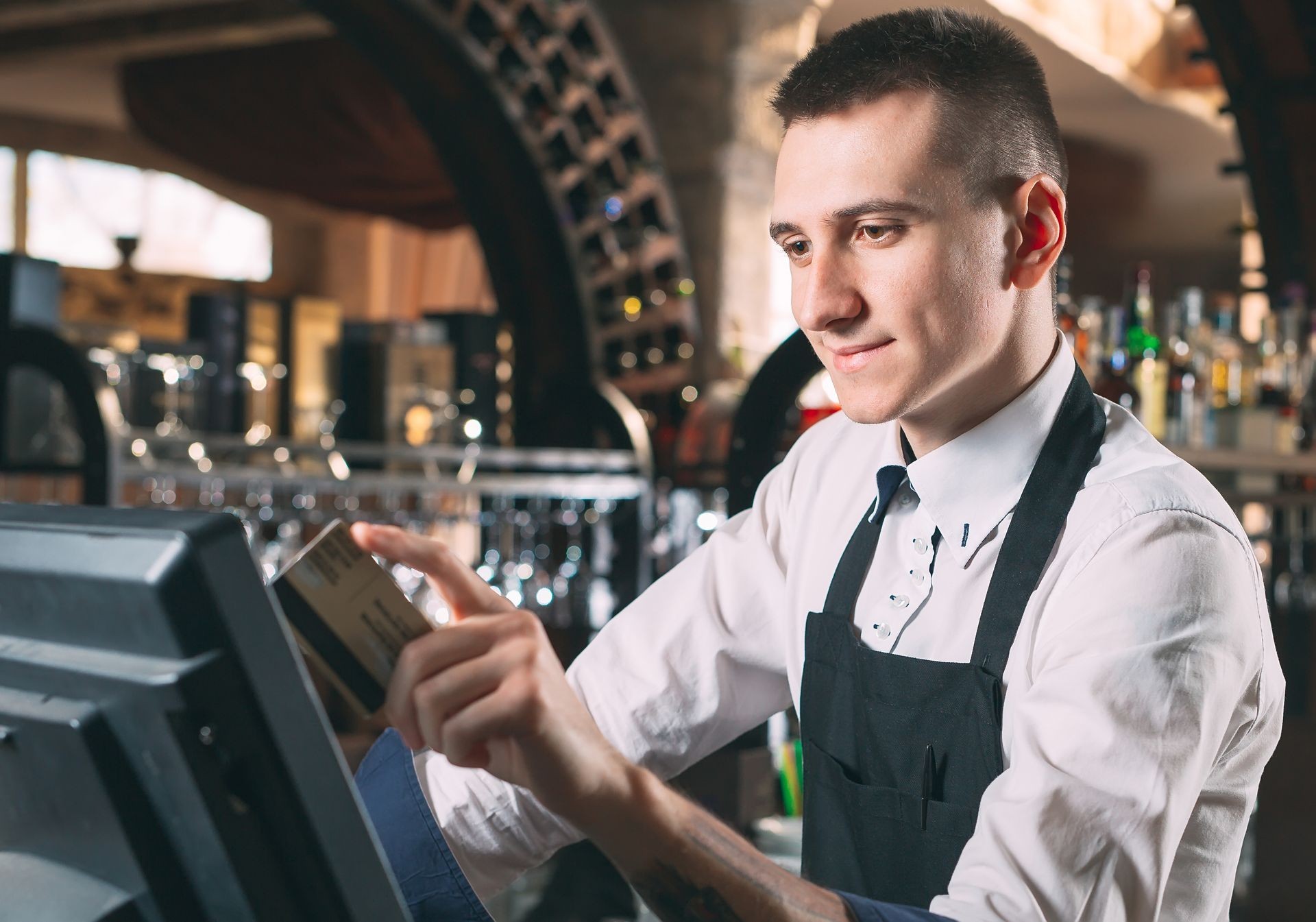small business, people and service concept - happy man or waiter in apron at counter with cashbox working at bar or coffee shop small business, people and service concept - happy man or waiter in apron at counter with cashbox working at bar or coffee shop